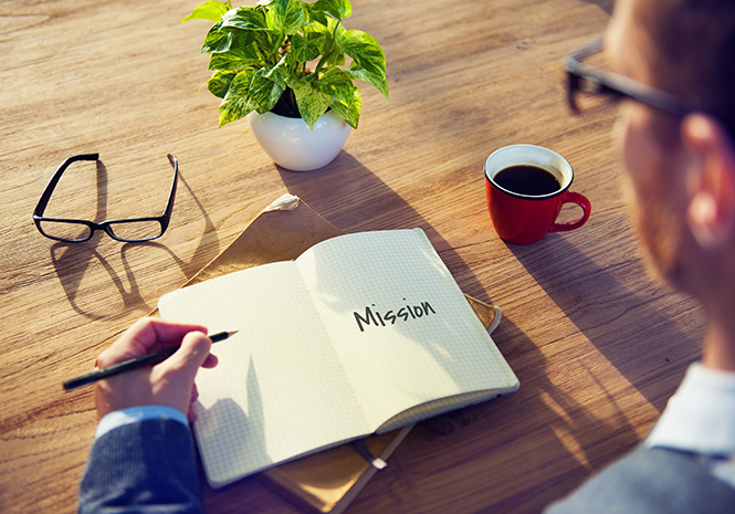 Open notebook with 'Mission' written, coffee and glasses on desk